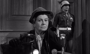 Movie still from “Judgment at Nuremberg” (1961), directed by Stanley Kramer – An older woman wearing a hat sitting in front of a microphone; Medium shot, Low angle