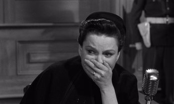 Movie still from “Judgment at Nuremberg” (1961), directed by Stanley Kramer – A woman in a black outfit covering her mouth with her hand; Close Up shot, Over the shoulder angle