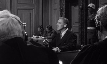 Movie still from “Judgment at Nuremberg” (1961), directed by Stanley Kramer – A man sitting in a chair in front of two other people; Medium shot, Over the shoulder angle