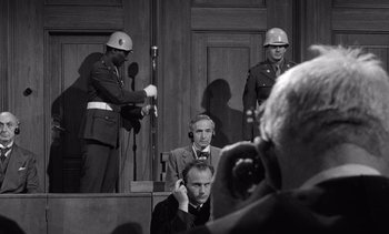 Movie still from “Judgment at Nuremberg” (1961), directed by Stanley Kramer – A man in a suit sitting in front of two men in military uniforms; Medium shot, Over the shoulder angle