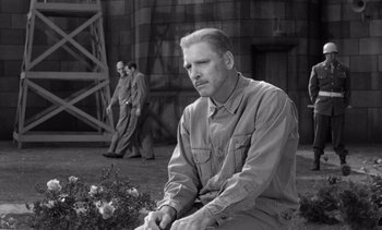 Movie still from “Judgment at Nuremberg” (1961), directed by Stanley Kramer – A man sitting on the ground in front of a building; Medium shot, Over the shoulder angle