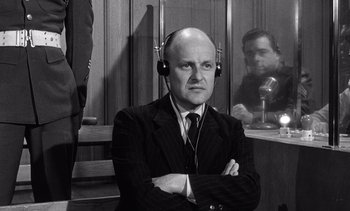 Movie still from “Judgment at Nuremberg” (1961), directed by Stanley Kramer – An old photo of a man wearing headphones in front of microphones; Medium shot, Over the shoulder angle