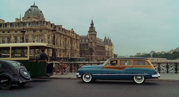 Movie still from “Julie & Julia” (2009), directed by Nora Ephron – An old car driving down a street past a building; Extreme Wide shot, Low angle