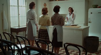 Movie still from “Julie & Julia” (2009), directed by Nora Ephron – A group of women standing in front of a counter; Wide shot, Low angle