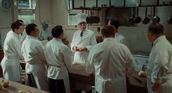 Movie still from “Julie & Julia” (2009), directed by Nora Ephron – A group of men standing around a table in a kitchen; Medium shot, Over the shoulder angle