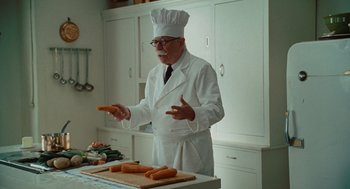 Movie still from “Julie & Julia” (2009), directed by Nora Ephron – An older man in a chef's outfit is making carrots; Medium shot, Over the shoulder angle