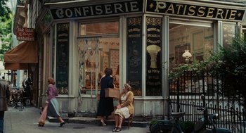 Movie still from “Julie & Julia” (2009), directed by Nora Ephron – Two women sitting on a bench in front of a store; Wide shot, High angle