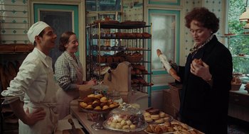 Movie still from “Julie & Julia” (2009), directed by Nora Ephron – Two women in aprons are standing in front of a table full of baked goods; Medium shot, Over the shoulder angle