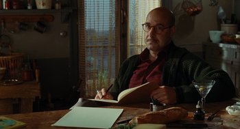 Movie still from “Julie & Julia” (2009), directed by Nora Ephron – A man sitting at a wooden table with a book; Medium shot, Over the shoulder angle