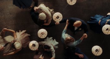 Movie still from “Julie & Julia” (2009), directed by Nora Ephron – A group of people sitting on the ground holding fans; Wide shot, Overhead angle