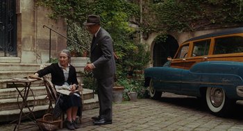 Movie still from “Julie & Julia” (2009), directed by Nora Ephron – An older man and woman sitting on a bench in front of an old car; Wide shot, Over the shoulder angle