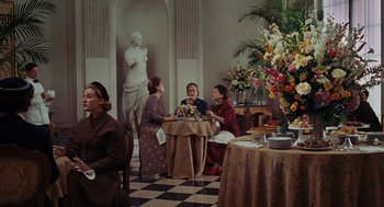 Movie still from “Julie & Julia” (2009), directed by Nora Ephron – A group of people sitting at a table with a vase of flowers in front of them; Wide shot, Over the shoulder angle