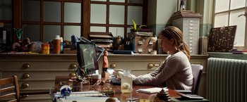 Movie still from “Juliet, Naked” (2018), directed by Jesse Peretz – A woman sitting at a desk in front of a computer; Medium shot, High angle