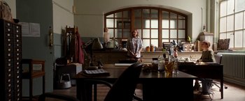 Movie still from “Juliet, Naked” (2018), directed by Jesse Peretz – A woman standing in front of a table in a room; Wide shot, Over the shoulder angle