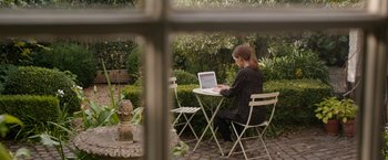 Movie still from “Juliet, Naked” (2018), directed by Jesse Peretz – A woman sitting at a table using a laptop computer; Wide shot, High angle