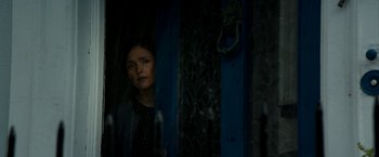 Movie still from “Juliet, Naked” (2018), directed by Jesse Peretz – A woman standing in a dark room looking out of a window; Close Up shot, Over the shoulder angle
