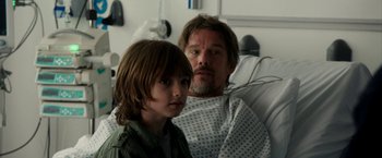 Movie still from “Juliet, Naked” (2018), directed by Jesse Peretz – A man and a boy sitting in a hospital bed; Medium shot, Over the shoulder angle