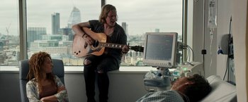 Movie still from “Juliet, Naked” (2018), directed by Jesse Peretz – A man playing an acoustic guitar in front of a computer monitor; Medium shot, Over the shoulder angle