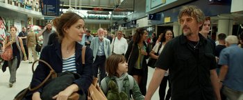 Movie still from “Juliet, Naked” (2018), directed by Jesse Peretz – A crowd of people walking through an airport terminal; Medium shot, Over the shoulder angle