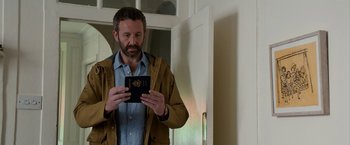 Movie still from “Juliet, Naked” (2018), directed by Jesse Peretz – A man holding a passport in his hands; Medium shot, Over the shoulder angle