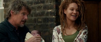 Movie still from “Juliet, Naked” (2018), directed by Jesse Peretz – A woman holding a baby in her arms and smiling; Medium shot, Low angle