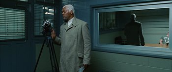 Movie still from “Jumper” (2008), directed by Doug Liman – An older man in a trench coat is walking in a building; Medium shot, Over the shoulder angle
