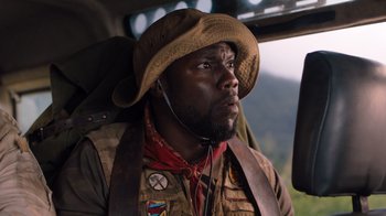 Movie still from “Jumanji: Welcome to the Jungle” (2017), directed by Jake Kasdan – A man with a hat and a microphone in a vehicle; Close Up shot, Over the shoulder angle