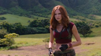 Movie still from “Jumanji: Welcome to the Jungle” (2017), directed by Jake Kasdan – A woman in a red top holding a gun in a field; Medium shot, Over the shoulder angle