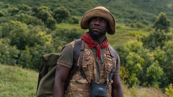 Movie still from “Jumanji: Welcome to the Jungle” (2017), directed by Jake Kasdan – A man with a hat and a camera in a field; Medium shot, Low angle