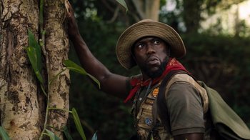 Movie still from “Jumanji: Welcome to the Jungle” (2017), directed by Jake Kasdan – A man wearing a hat leaning up against a tree; Close Up shot, Low angle