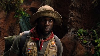 Movie still from “Jumanji: Welcome to the Jungle” (2017), directed by Jake Kasdan – A man wearing a hat and vest in front of rocks; Close Up shot, Low angle