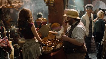 Movie still from “Jumanji: Welcome to the Jungle” (2017), directed by Jake Kasdan – A man and a woman are eating bread at an outdoor market; Medium shot, Over the shoulder angle