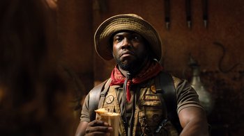 Movie still from “Jumanji: Welcome to the Jungle” (2017), directed by Jake Kasdan – A man holding a donut while wearing a hat; Close Up shot, Low angle