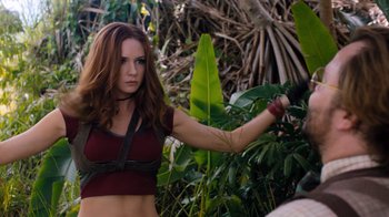 Movie still from “Jumanji: Welcome to the Jungle” (2017), directed by Jake Kasdan – A beautiful woman holding a sword in the woods; Medium shot, Over the shoulder angle