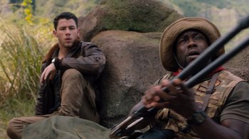 Movie still from “Jumanji: Welcome to the Jungle” (2017), directed by Jake Kasdan – Two men sitting next to each other holding guns; Close Up shot, Over the shoulder angle