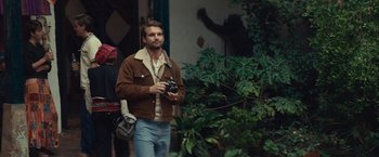 Movie still from “Jungle” (2017), directed by Greg McLean – A man holding a camera while standing next to a bush; Medium shot, Over the shoulder angle