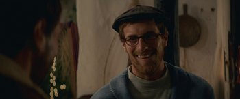 Movie still from “Jungle” (2017), directed by Greg McLean – A man wearing glasses and a hat smiling for the camera; Close Up shot, Over the shoulder angle
