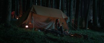 Movie still from “Jungle” (2017), directed by Greg McLean – A woman sitting under a tarp in the woods at night; Wide shot, Low angle