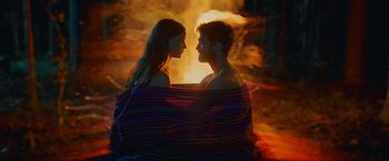 Movie still from “Jungle” (2017), directed by Greg McLean – A man and a woman sitting on a blanket in front of a fire; Medium shot, High angle