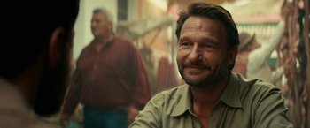 Movie still from “Jungle” (2017), directed by Greg McLean – A man with a goatee smiles for the camera; Close Up shot, Over the shoulder angle