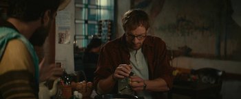 Movie still from “Jungle” (2017), directed by Greg McLean – A man in glasses and a red shirt is putting something in a jar; Medium shot, Low angle