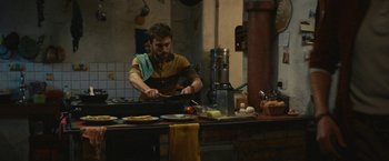 Movie still from “Jungle” (2017), directed by Greg McLean – A man in a kitchen preparing food on a stove; Medium shot, High angle