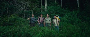 Movie still from “Jungle” (2017), directed by Greg McLean – A group of men standing next to each other in the woods; Wide shot, High angle