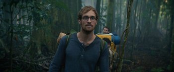 Movie still from “Jungle” (2017), directed by Greg McLean – A man with a beard wearing glasses and a blue shirt; Close Up shot, Low angle