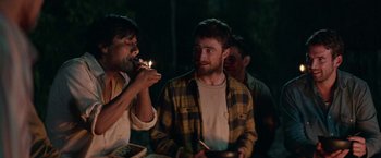 Movie still from “Jungle” (2017), directed by Greg McLean – A man lighting a candle on top of a cake while another man looks on; Medium shot, Over the shoulder angle