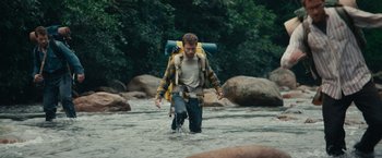 Movie still from “Jungle” (2017), directed by Greg McLean – A man walking through a river with a backpack; Wide shot, High angle