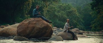 Movie still from “Jungle” (2017), directed by Greg McLean – Two men sitting on a rock in a river; Wide shot, Over the shoulder angle