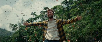 Movie still from “Jungle” (2017), directed by Greg McLean – A man standing in front of a tree with his arms outstretched; Medium shot, Low angle