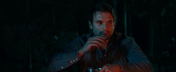 Movie still from “Jungle” (2017), directed by Greg McLean – A man sitting at a table with a drink in front of him; Close Up shot, Over the shoulder angle