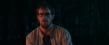 Movie still from “Jungle” (2017), directed by Greg McLean – A man wearing glasses and a striped shirt is looking at the camera; Close Up shot, Over the shoulder angle